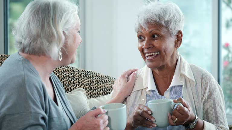 Two senior women conversing on sofa, with coffee