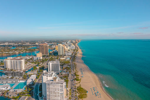 Waterfront hotels and resorts line up in front of the white sand beach on this gorgeous morning in Fort Lauderdale with waterway in frame and palm trees lining up the beach