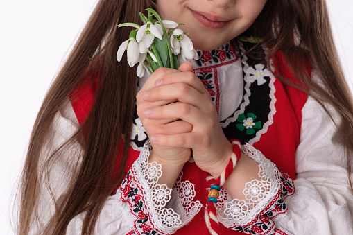 Bulgarian woman in traditional folklore costume nosia, bouquet spring flowers snowdrops and martenitsa symbol of March Baba Marta holiday, Bulgaria