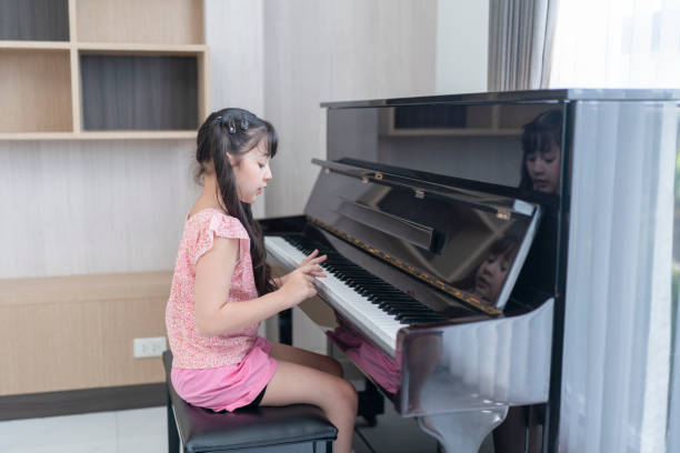 little asian girl plays a grand piano. Preschool child learning to play music instrument. little asian girl plays a grand piano. Preschool child learning to play music instrument. girl playing piano stock pictures, royalty-free photos & images