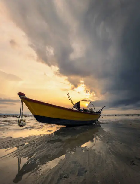 Lone fishing boat on the beach at low tide during colorful sunset