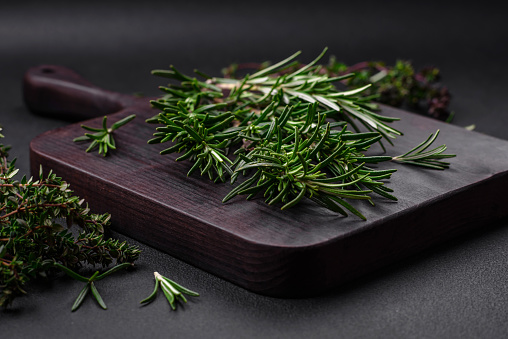 Sprigs of fresh green rosemary on a wooden cutting board on a dark concrete background