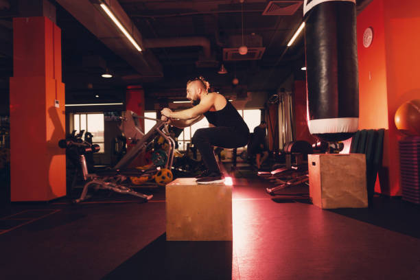 A man with a beard does an exercise jump on a pedestal in the gym. A man with a beard does an exercise jump on a pedestal in the gym burpee stock pictures, royalty-free photos & images