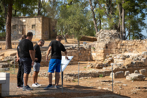 Group of people visiting archeological site and remains of ancient Sparta city located on Peloponnese peninsula, south Greece. They are reading information sign.