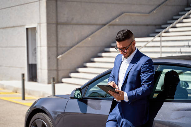 istock Executive smiling Caucasian male, leaning on car and using tablet 1472036242