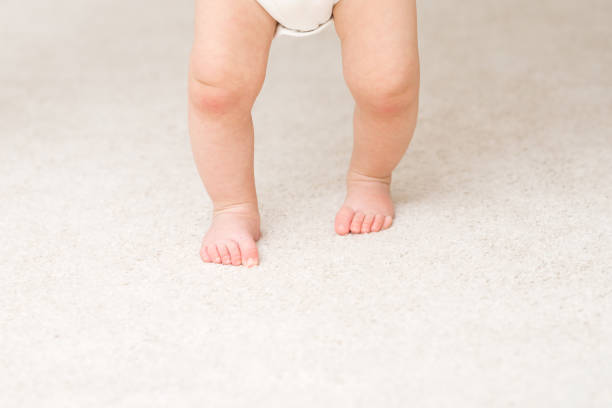 istock Baby barefoot on light soft carpet. Closeup. First steps. Front view. 1472039811