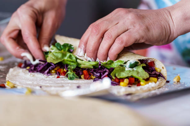 A woman is making tortillas filled with meat and vegetables.