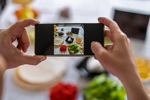 A young female chef is preparing a banquet table while making delicious Mexican food and using a mobile phone to take a picture.