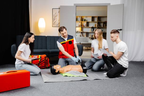 istock Young man instructor helping to make first aid heart compressions with dummy during the group training indoors 1472041176