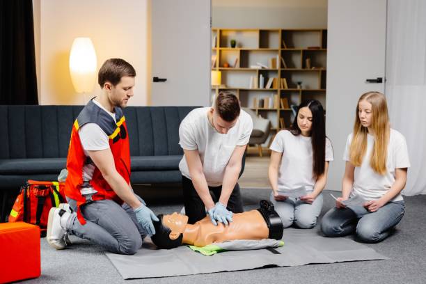 istock Young man instructor helping to make first aid heart compressions with dummy during the group training indoors 1472041187