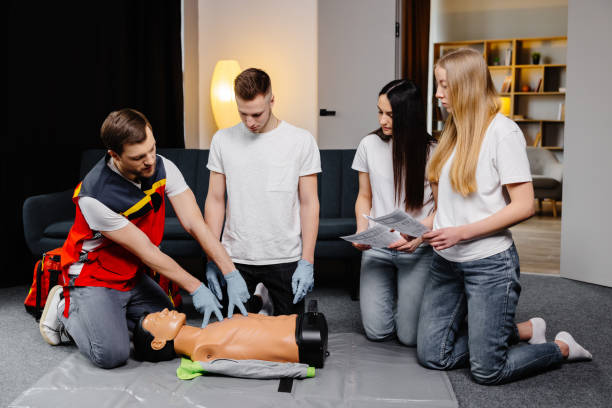 istock Young man instructor helping to make first aid heart compressions with dummy during the group training indoors 1472041188