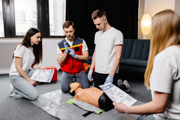 istock Young man instructor helping to make first aid heart compressions with dummy during the group training indoors 1472041189