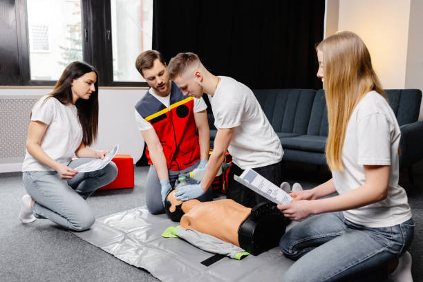 istock Young man instructor helping to make first aid heart compressions with dummy during the group training indoors 1472041193
