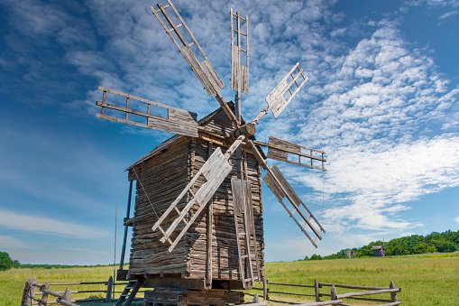 Old wooden windmill on the green meadow with scenic blue sky on the background.