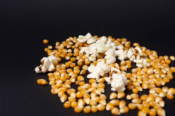 grãos de milho para fazer pipoca e vários pedaços de pipoca pronta. - popcorn black dietary fiber refreshment - fotografias e filmes do acervo