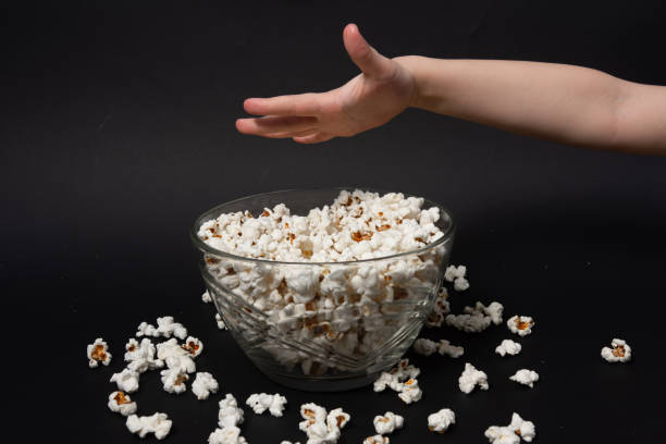 a mão de uma criança em um fundo preto leva pipoca de uma tigela - popcorn black dietary fiber refreshment - fotografias e filmes do acervo