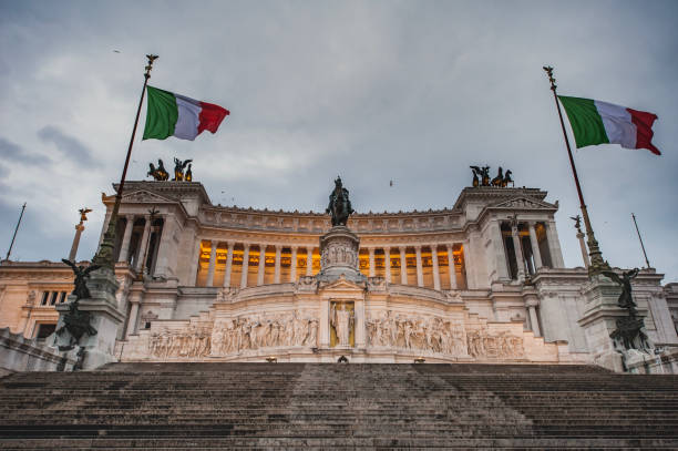 Dusk view of Victor Emmanuel II National Monument (Monumento Nazionale a Vittorio Emanuele secondo) with fluttering Italian flags. Historical building Vittoriano or Altare della Patria is a fine example of Italian revival or renaissance architecture vista al atardecer del monumento nacional victor emmanuel ii (monumento nazionale a vittorio emanuele secondo) con banderas italianas ondeando. el edificio histórico vittoriano o altare della patria es un buen ejemplo de renacimiento italiano o arquitectu