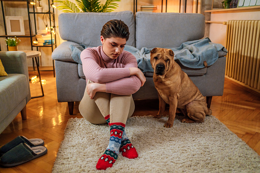 Sad young woman sitting on the floor at home. Her shar-pei dog is sitting next to her