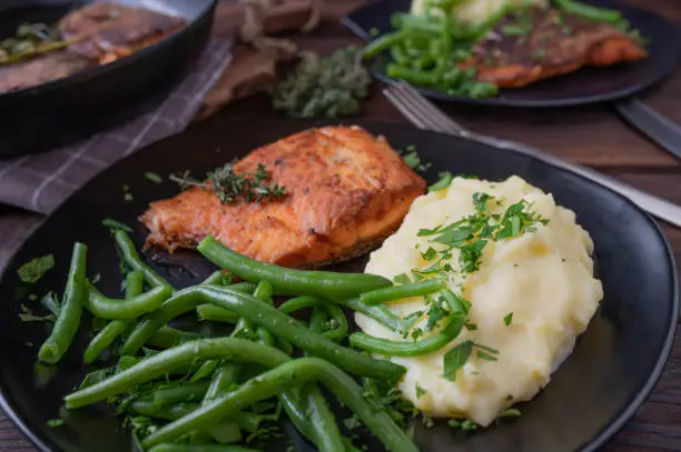 Delicious salmon dish with green beans and potato puree. Served ready to eat on a brown plate on rustic and wooden table background. Closeup
