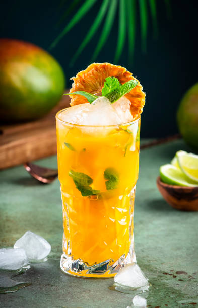 Alcoholic cocktail with vodka, pineapple juice, mango, liquor, ice. Long drink or summer mocktail. Tropical dark background with palm leaves and exotic fruits Alcoholic cocktail with vodka, pineapple juice, mango, liquor, ice. Long drink or summer cold mocktail. Tropical dark background with palm leaves and exotic fruits mai tai stock pictures, royalty-free photos & images