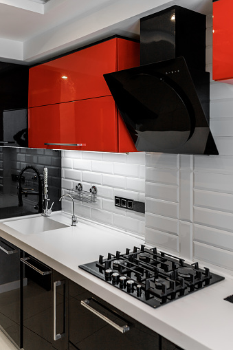 Modern kitchen interior with red and black cabinets and white ceramic floor.