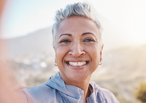Elderly woman runner, training selfie and smile in nature for retirement fitness, wellness or self care. Happy senior black woman, park portrait and running by mountains, outdoor and summer workout