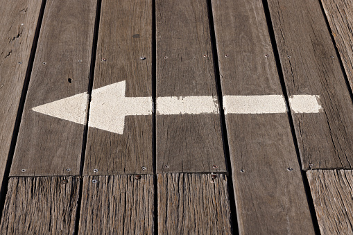Pointed directional arrow on a wooden deck.