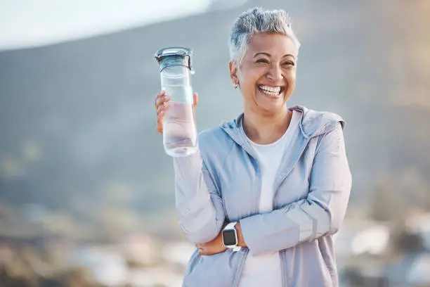 Photo of Fitness, happy or old woman with water bottle in nature to start training, exercise or hiking workout in New Zealand. Portrait, liquid or healthy senior person smiles with pride, goals or motivation