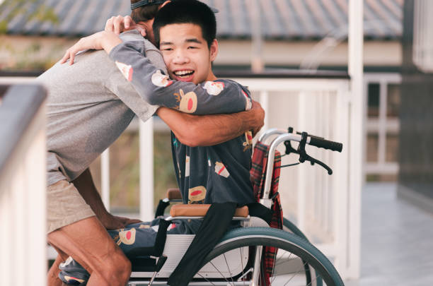 Teenager boy on wheelchair in the outdoor activity, Family Caregiving and diverse family concept. Young man with disability on wheelchair and father or volunteer or caregiver at happy time in the house, Caring for love and positive energy from parents, mental health, Family Caregiving concept. wheelchair lift stock pictures, royalty-free photos & images