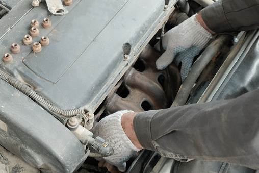 An auto mechanic installs an exhaust manifold on the engine of a passenger car.