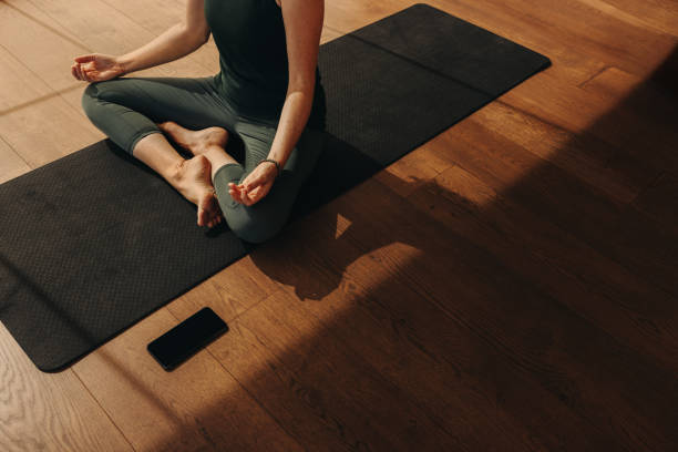 Hatha yoga at home High angle view of a senior woman meditating and practicing hatha yoga. Unrecognizable woman doing a breathing exercise while sitting in easy pose. Woman following a healthy fitness routine at home. yoga studio stock pictures, royalty-free photos & images