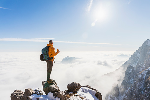 Hiker with yellow jacket on top of the mountain looking at the sea of clouds in the clean blue sky