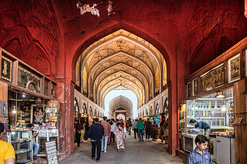 New Delhi, India, February 23rd, 2023: Indian people walking along covered arched called The Chhatta Chowk meaning Covered Bazaar at the entrance of Red Fort from Lahori Gate side. Souvenir shops market at both sides