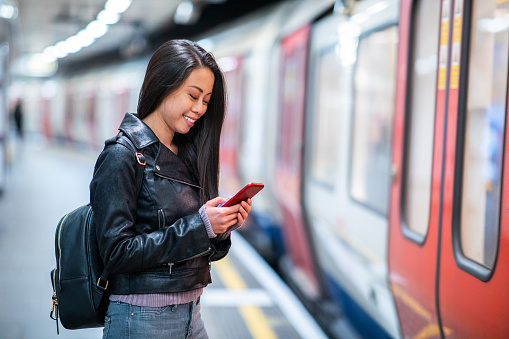 Chinese woman at underground train station using mobile phone - Young asian woman waiting for the train and smiling typing on the phone - Lifestyle and travel concepts