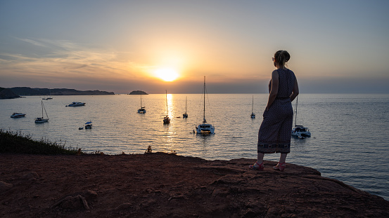 Young blonde girl enjoying the sunset over the cliff of Cala Cavallería, Menorca, Balearic Islands, Spain