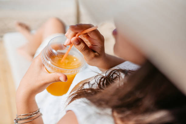istock Young Woman Drinking Orange Juice By The Beach 1472068004