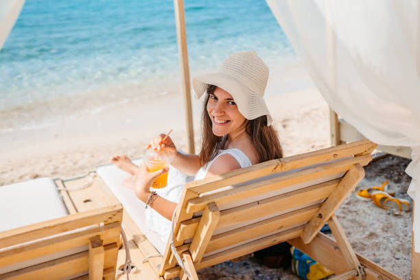 istock Young Woman Drinking Orange Juice By The Beach 1472068051