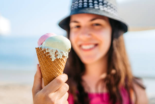 Young Woman Holding Ice Cream On The Beach Close-up of a ice cream being held by a young woman on the beach. licking ice cream cone stock pictures, royalty-free photos & images
