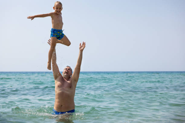 Caucasian father throwing his son in the air, while having a fun time while playing in the sea during their vacation
