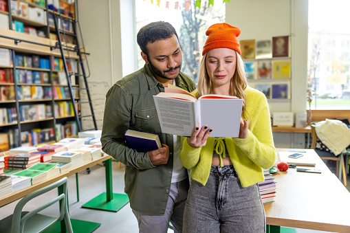 In the library. Young man and blonde woman reading book together