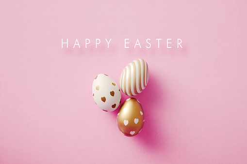 Gold painted Easter eggs and Happy Easter message on pink background. Horizontal composition with copy space. Easter concept.