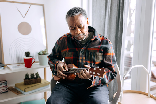 Casually clothed senior man playing ukulele at his apartment