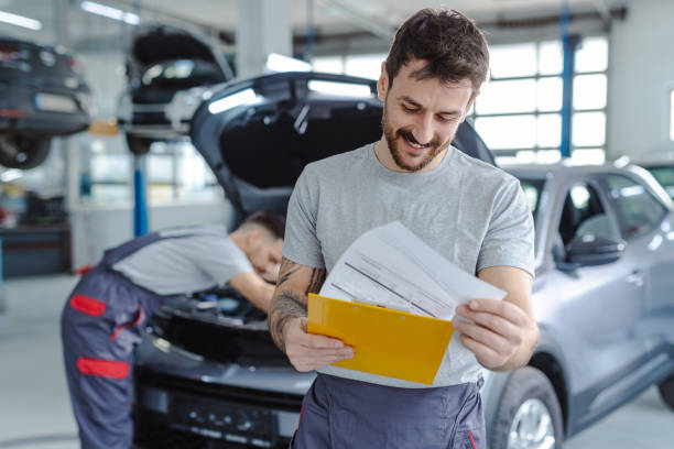 Automotive technician at auto service center Smiling automotive technician in auto service checking diagnostic papers Vehicle Servicing Reading stock pictures, royalty-free photos & images