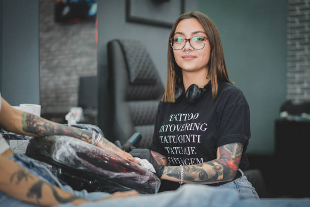 Tattoo artist young women posing for camera while tattooing
