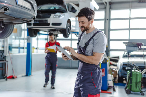 Automotive technicians at the service station Smiling auto mechanic in auto service holding digital tablet. In background is the other worker car mechanic stock pictures, royalty-free photos & images