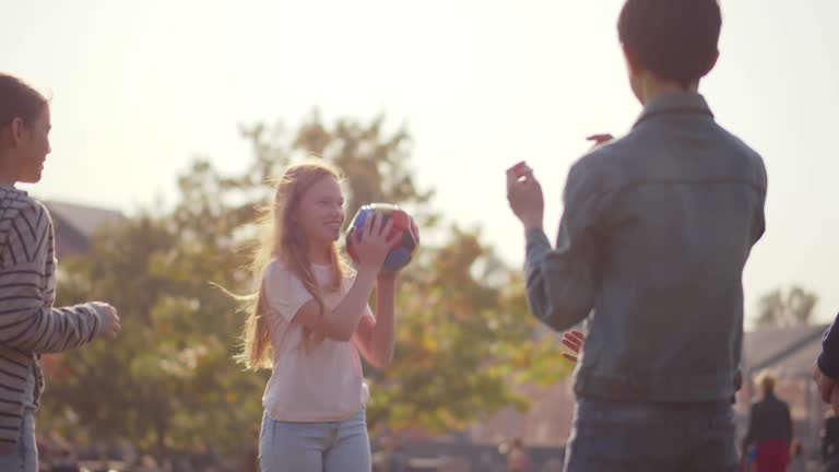 Diverse children play with ball in summer park. Realtime