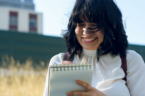 portrait of young latina woman of venezuelan ethnicity, happy smiling writing thought in a notebook, organizing ideas, students concept, copy space.