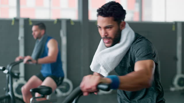 Exercise bike, fitness or towel with a man athlete sweating in a gym for cardiovascular workout. Elliptical machine, training and breathing with a male cycling to increase health, cardio or endurance