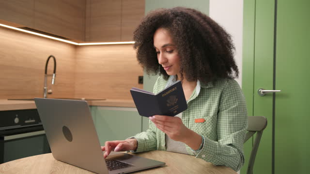 Mixed Race Woman Holding US Passport Using Laptop. Female filling application form holding ID document.