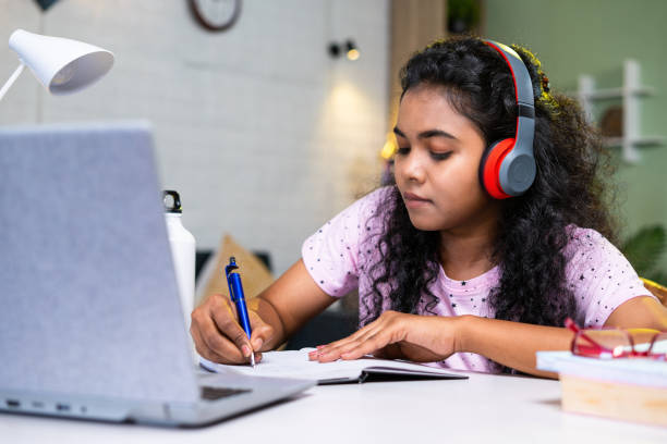 istock Girl student making notes from online class using laptop at home by wearing wireless headphones - concept of development, learning and technology. 1472090119